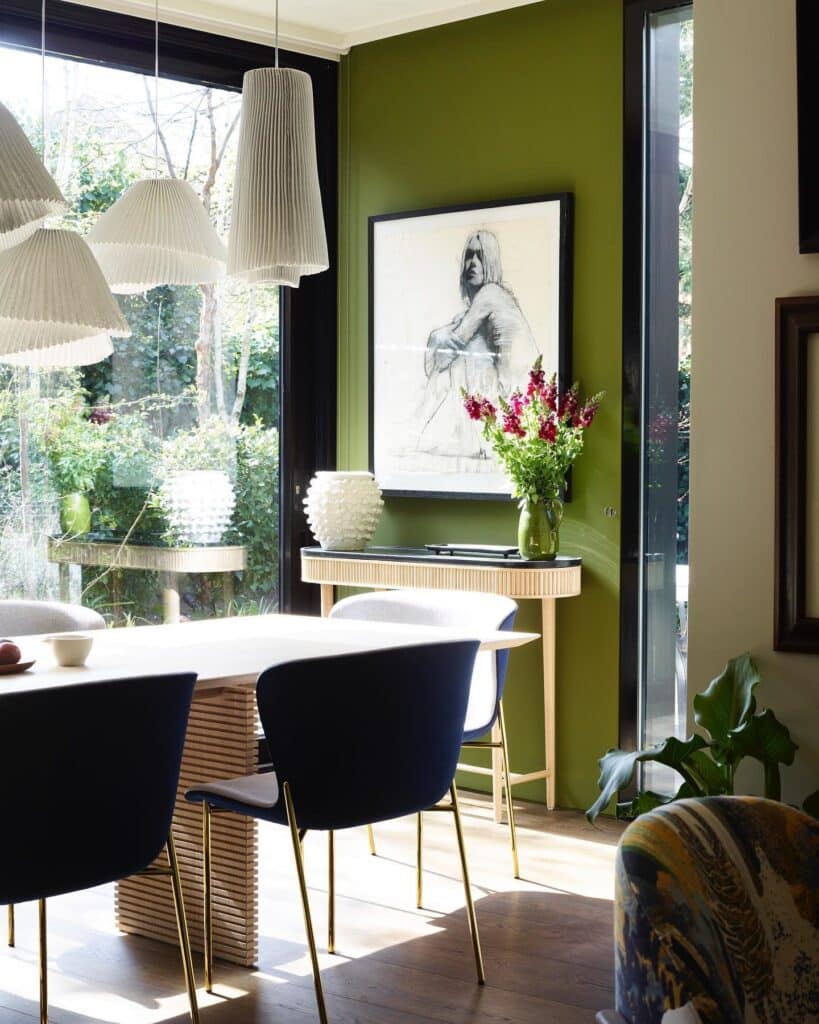 dining room with Farrow and Ball Bancha green feature wall, large figurative artwork above fluted sideboard and navy dining chairs
