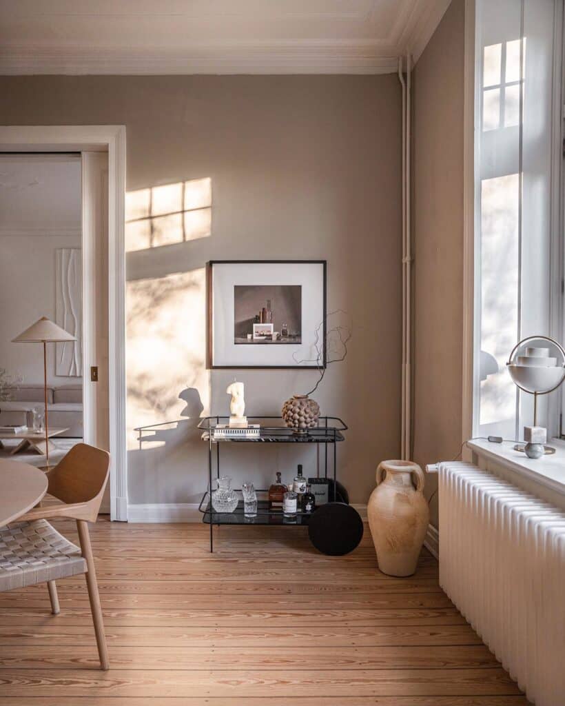 dining room corner with Farrow and Ball Drop Cloth walls, black metal bar trolley styled with glassware and artwork above