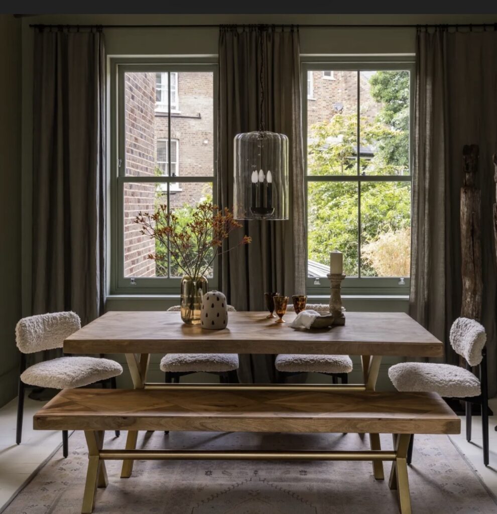 Atkin and Thyme Reeves large solid oak dining table with bench and boucle chairs in a dark green dining room with olive painted windows