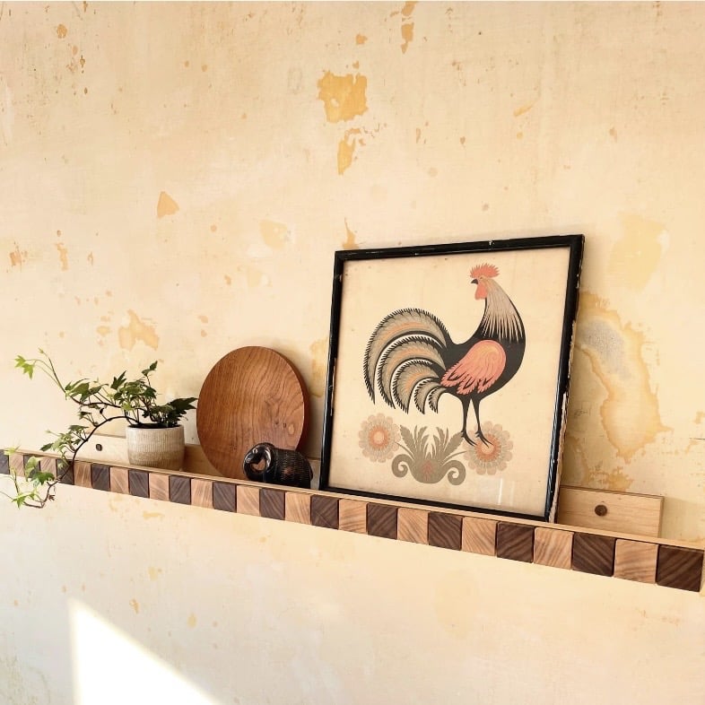 checkerboard ash and walnut floating picture shelf styled with folk art print and ceramics on a limewash wall