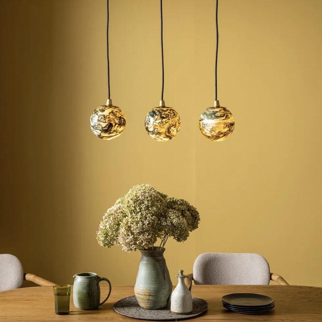Atkin and Thyme Tula Trio amber glass pendant lights over a dining table styled with ceramics and hydrangeas