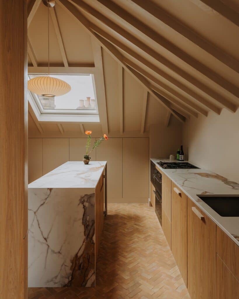 Japandi kitchen with oak cabinetry, marble waterfall island, herringbone parquet floor and paper pendant light painted in Farrow and Ball Archive