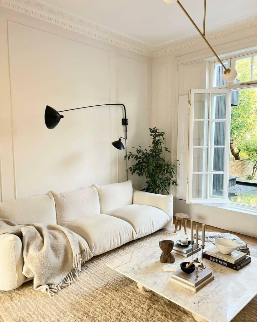 Minimalist japandi living room with low cloud sofa, marble coffee table, black wall sconce and tall sash windows painted in Farrow and Ball Wevet and All White