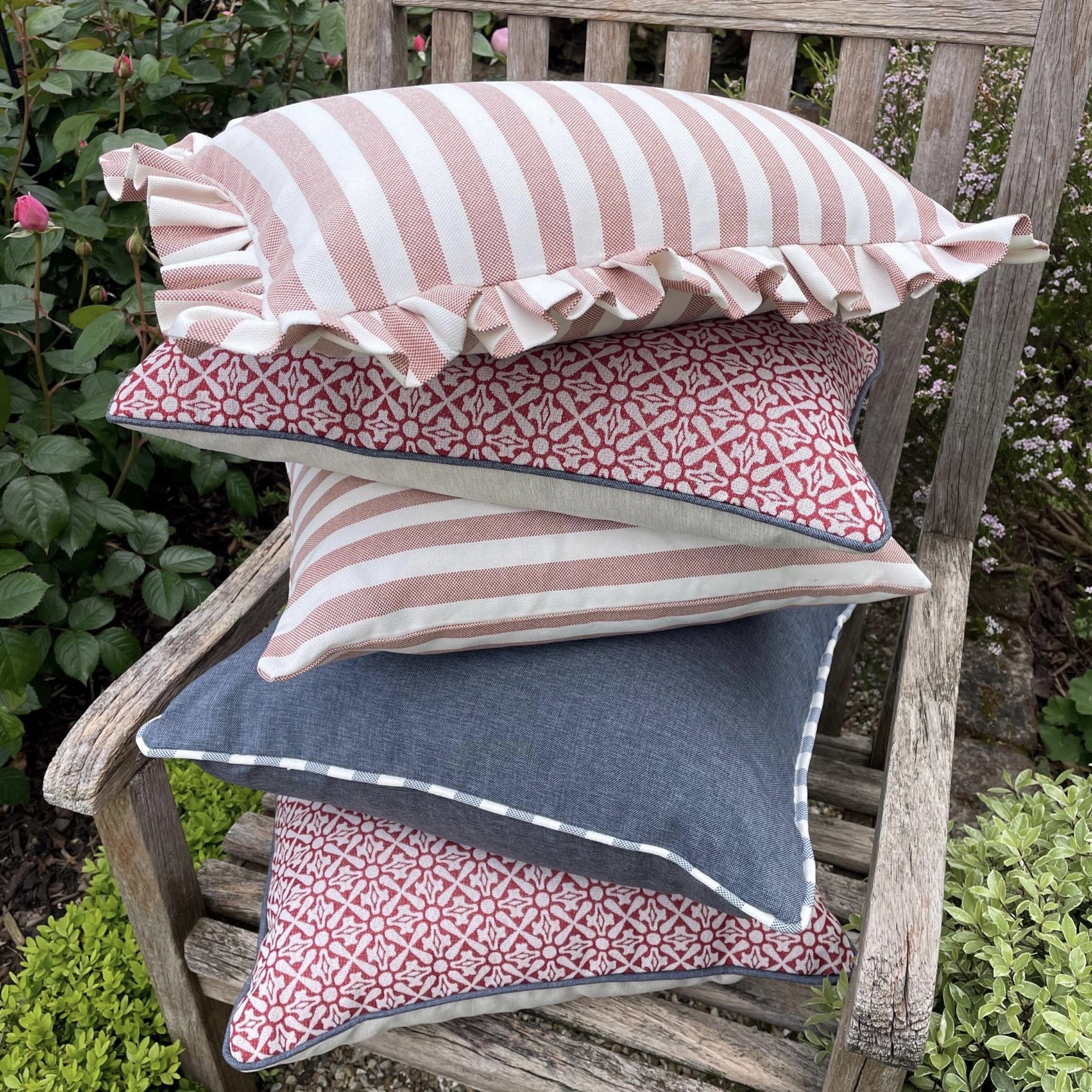 Stack of red and white striped outdoor garden cushions with ruffle edge on wooden garden bench by KerrisdaleHome
