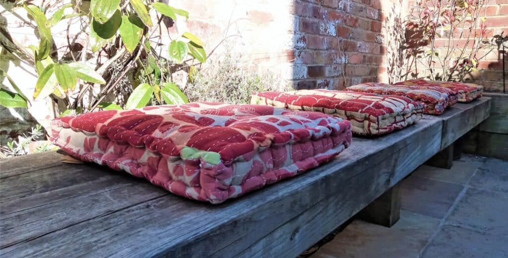 Kantha stitched floor cushions made from upcycled vintage sari fabric in warm mixed colours stacked on outdoor wooden bench
