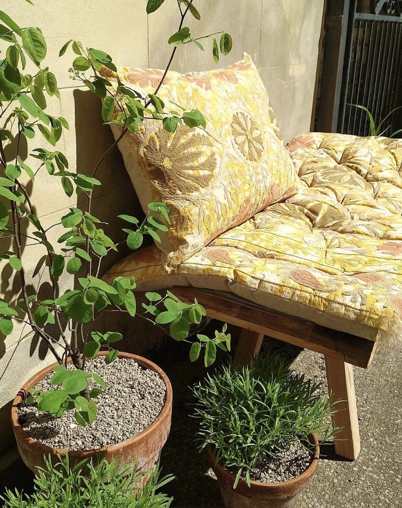 Hand embroidered suzani outdoor bench cushion in warm yellow rust and ochre floral motifs on natural cotton, styled on wooden garden bench
