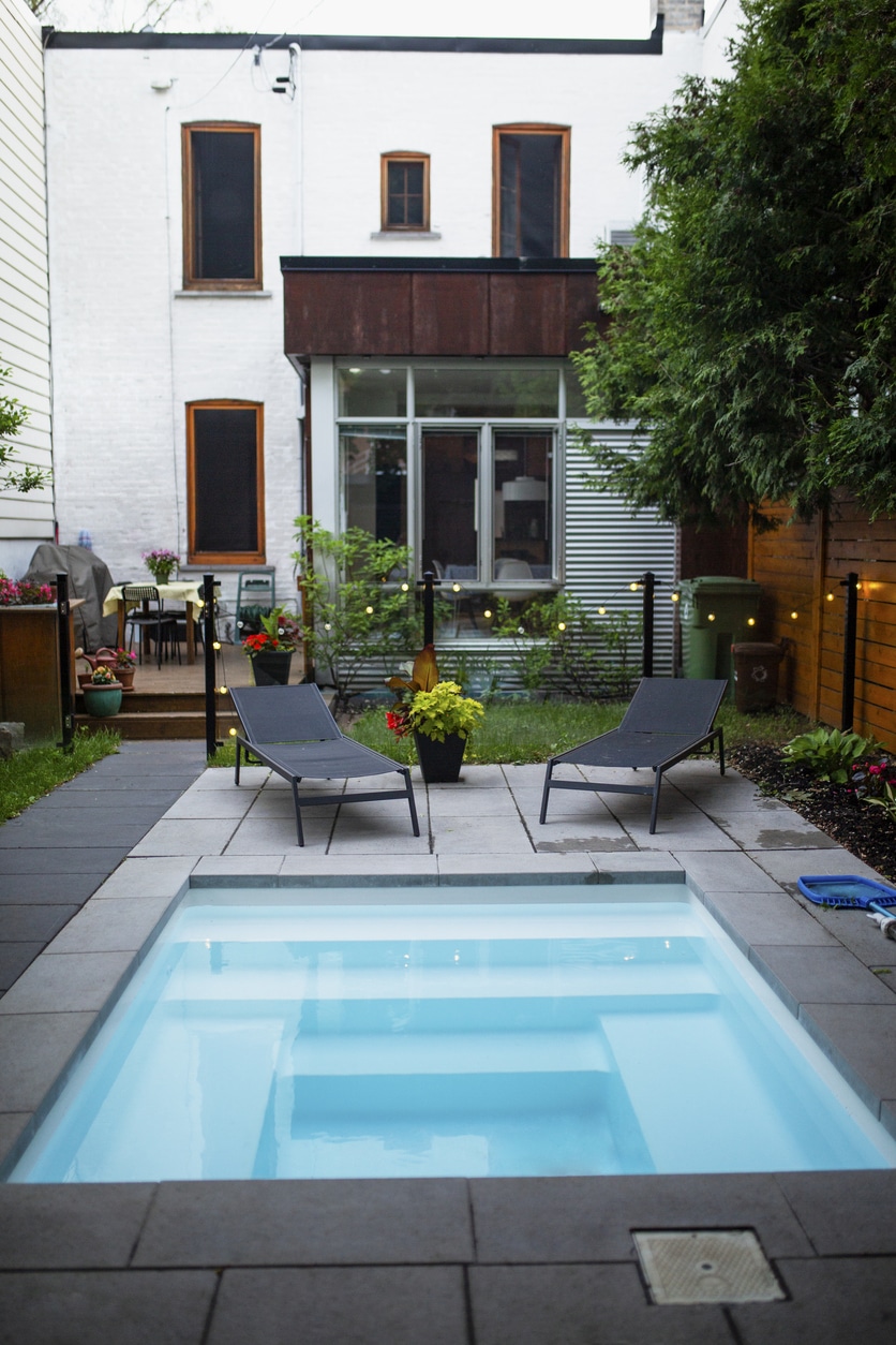 Small garden ideas UK: compact plunge pool with slate paving, sun loungers and festoon lights in an urban back garden
