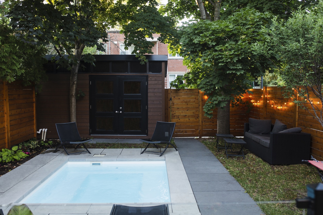 Small garden ideas UK: plunge pool with garden room, festoon lights and rattan seating area in a compact urban back garden
