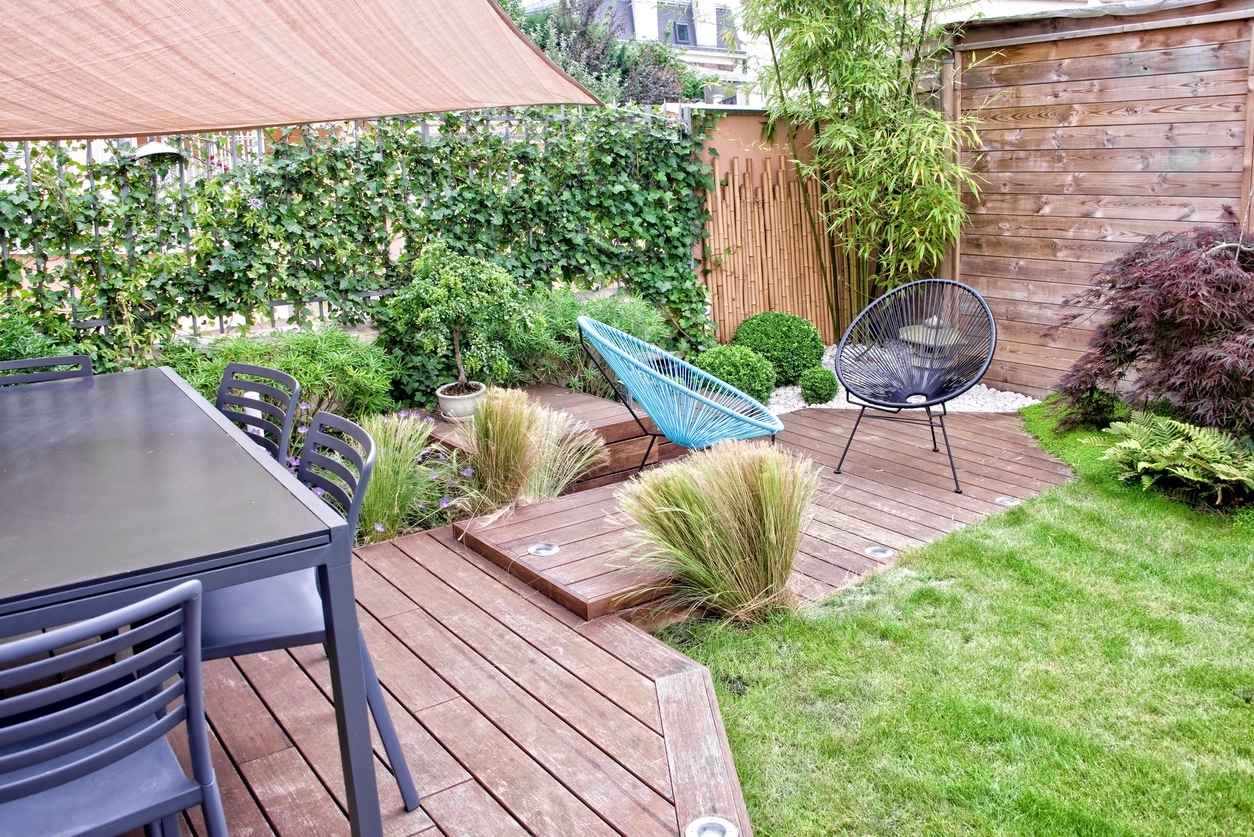 Small garden decking ideas: overhead view of modern timber deck with wire dining chairs, clipped box balls, ornamental grasses and bamboo screening