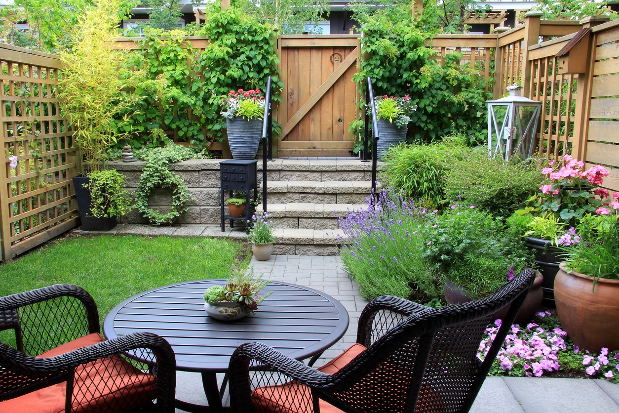 Small garden ideas UK: compact back garden with dark rattan dining furniture, paved path, lavender border and trellis fencing
