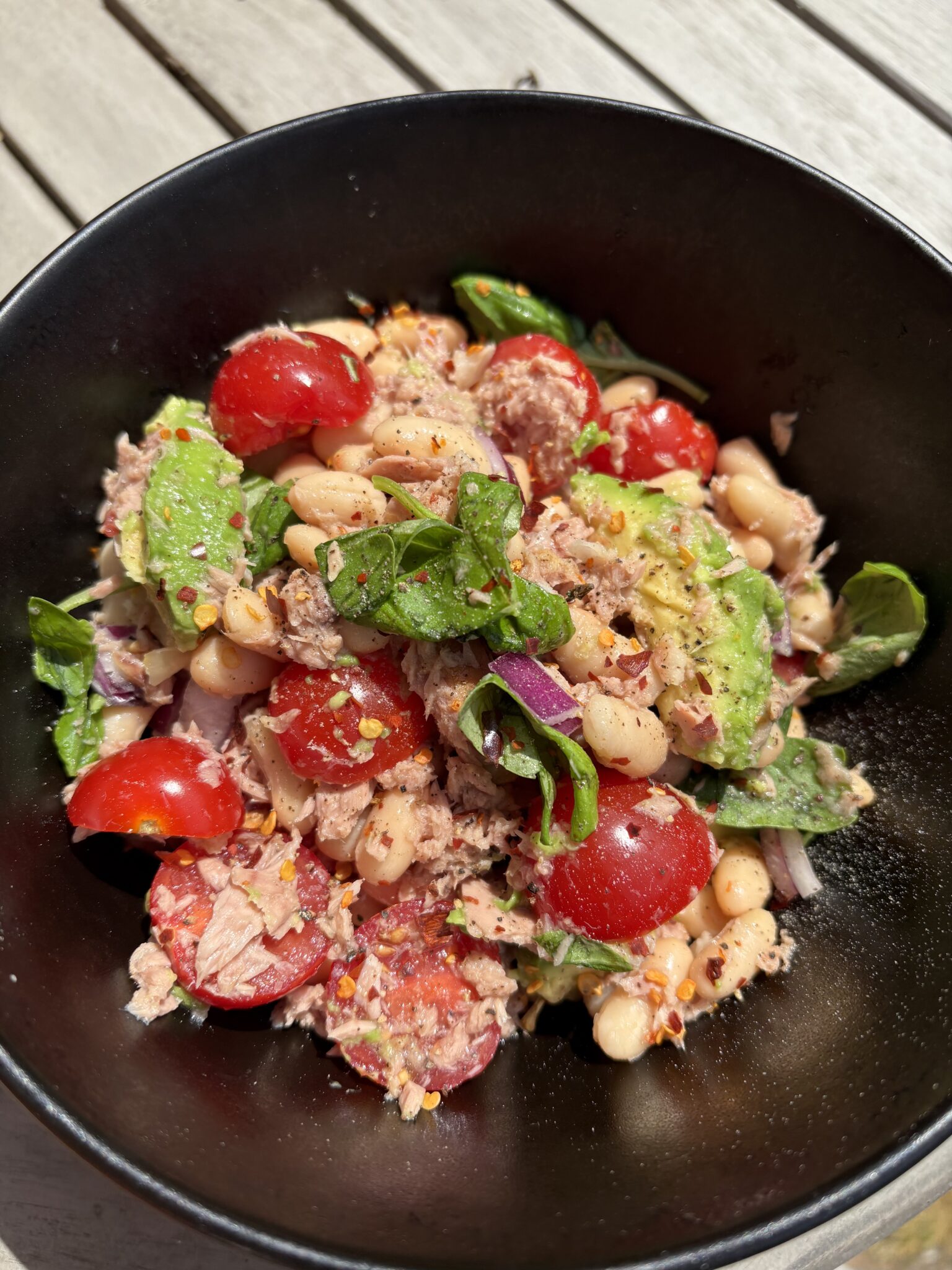 Tuna white bean and avocado salad with cherry tomatoes, chilli flakes and fresh basil in a black bowl