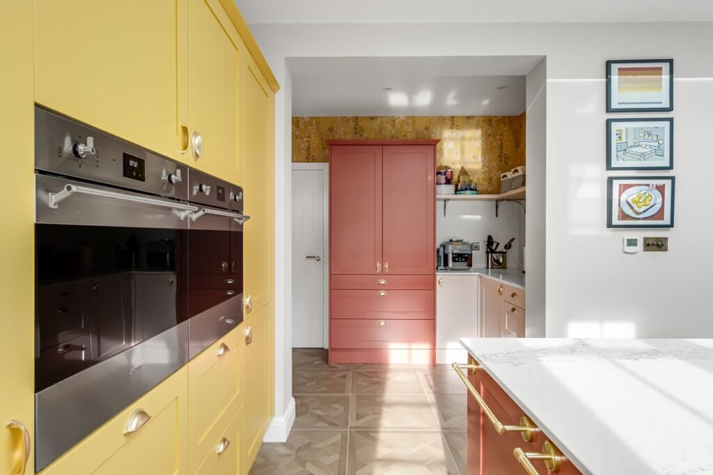 Yellow kitchen cabinets painted in Farrow & Ball Babouche with coral pink cabinetry, marble worktops and brass handles in a colourful modern kitchen