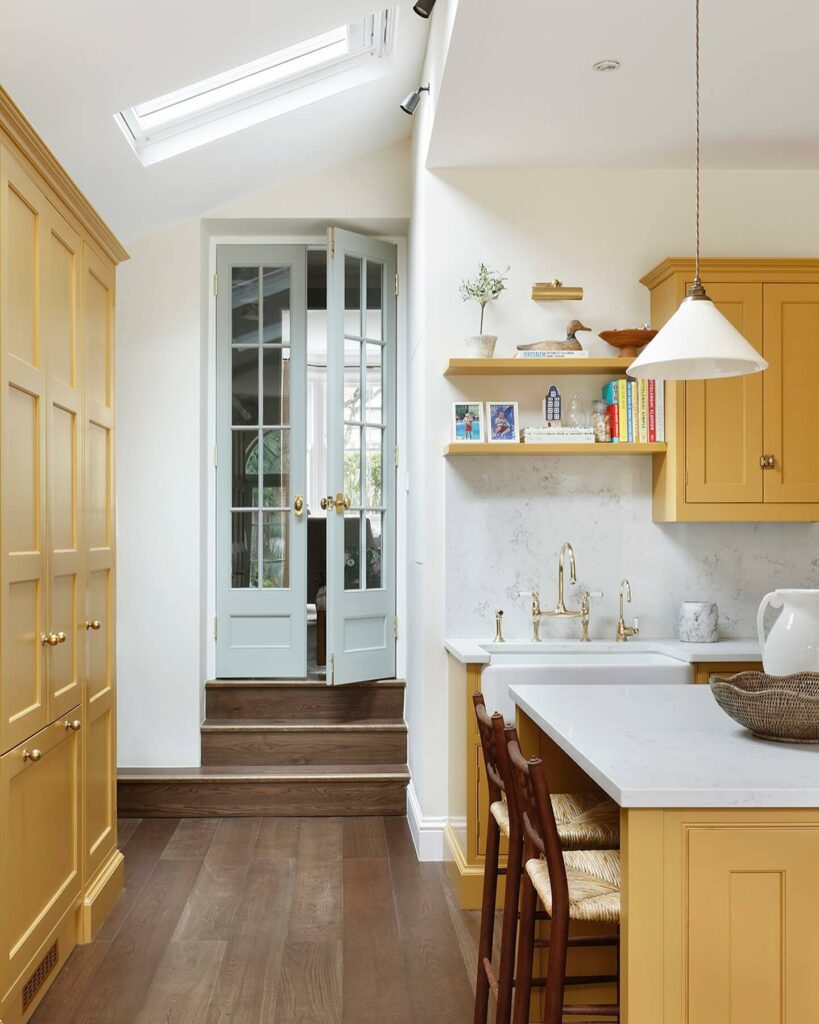 Butter yellow kitchen cabinets painted in Farrow & Ball India Yellow with pale blue doors, white worktops and warm wood flooring