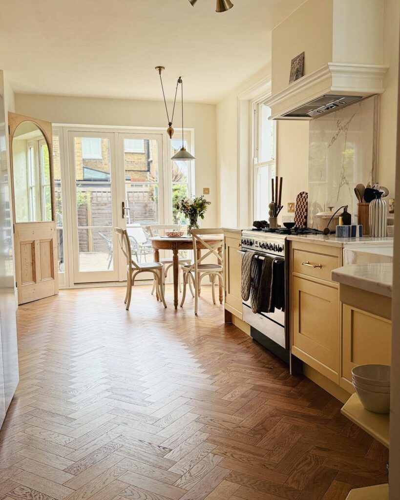 Soft yellow kitchen painted in Farrow & Ball Hay with herringbone wood flooring, cream walls and a light-filled dining area