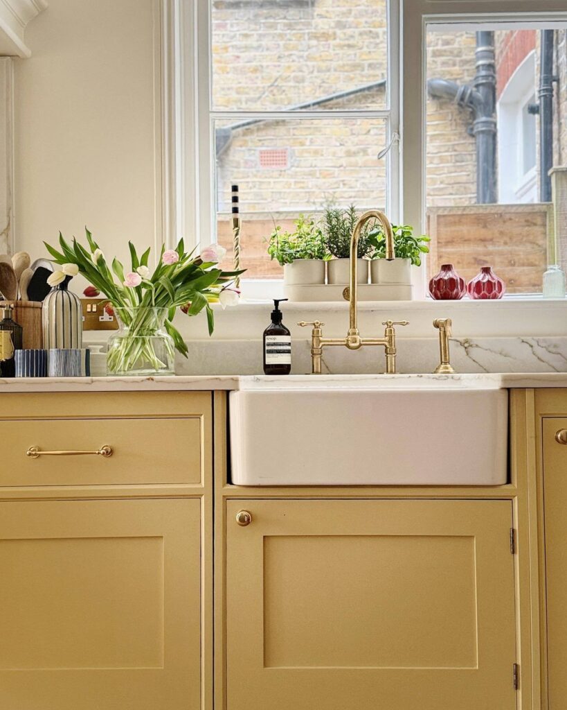 Soft yellow kitchen cabinets painted in Farrow & Ball Hay with brass taps, farmhouse sink and marble splashback