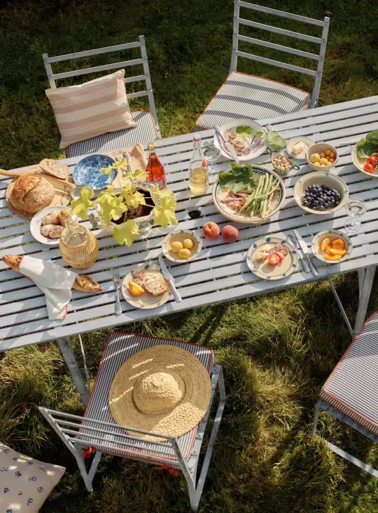 Rowen & Wren Sudbury Garden Dining Table laid for outdoor dining on a grass lawn with parasol and stripe cushions — outdoor dining ideas