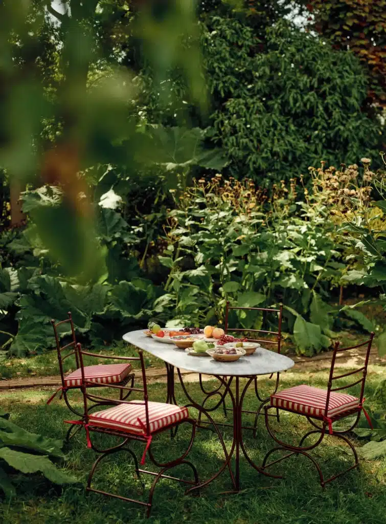 Rowen & Wren Sorrel Marble Dining Table in a lush garden setting with red stripe cushions — outdoor dining ideas
