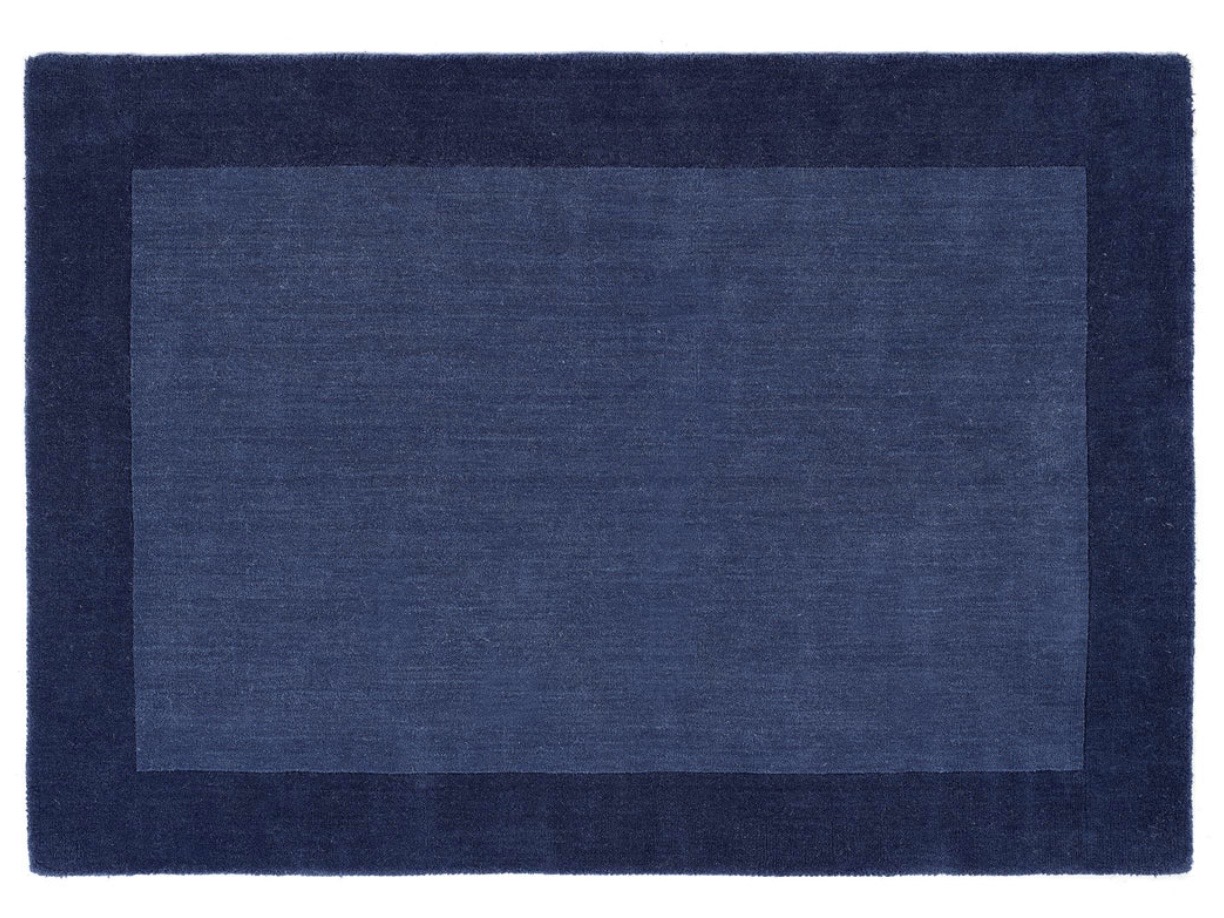 Navy bordered wool rug to ground a tan leather sofa living room — indigo blue contrast scheme