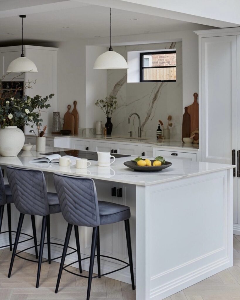 Two antique brass and translucent porcelain pendant lights hanging above a white marble kitchen island with grey upholstered bar stools