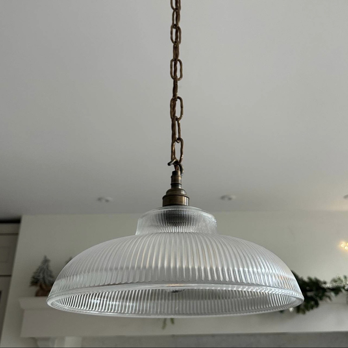 Close-up of a reeded glass pendant light shade with a twisted brass chain against a plain background