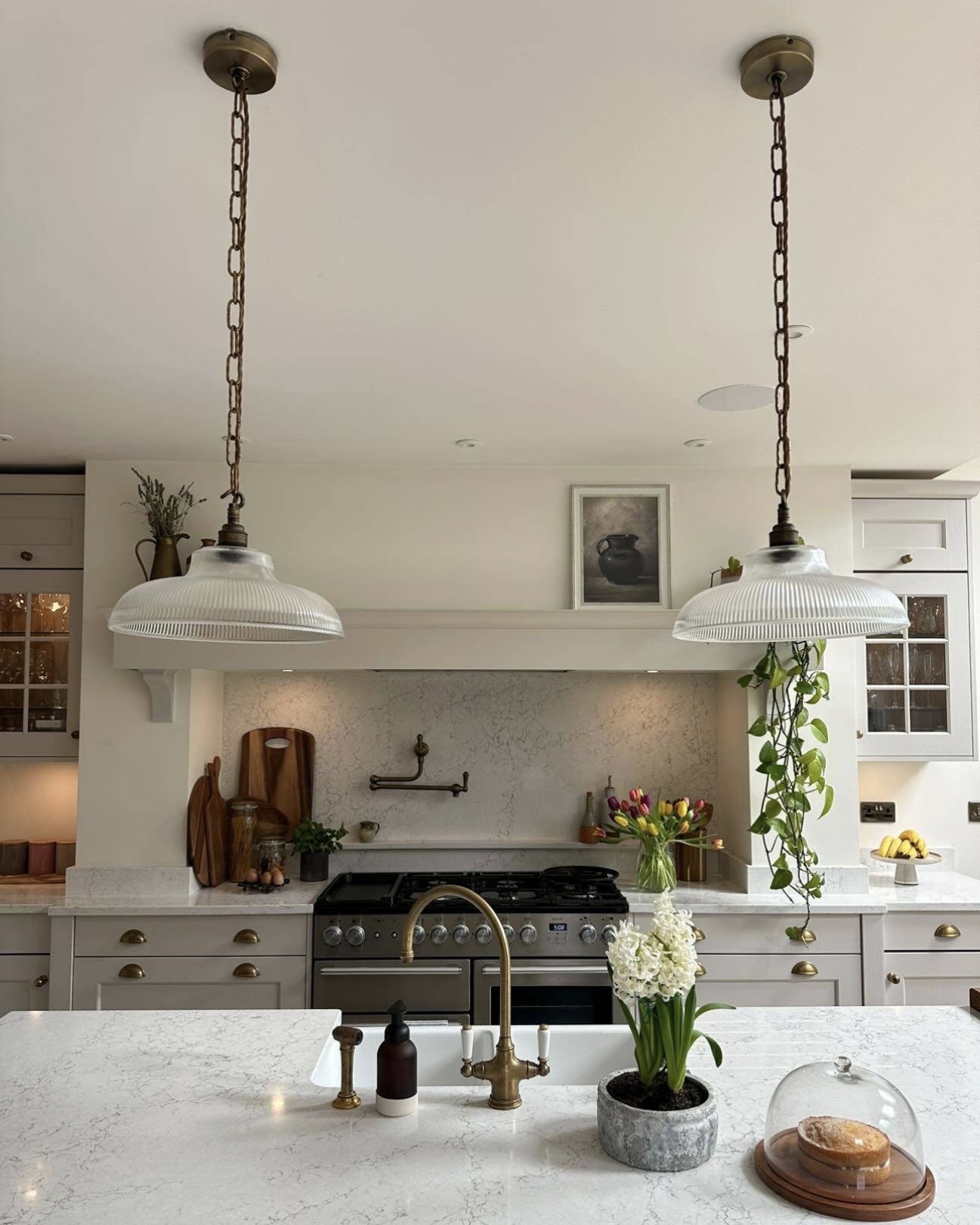 Two reeded glass pendant lights with twisted brass chains hanging over a white marble kitchen island
