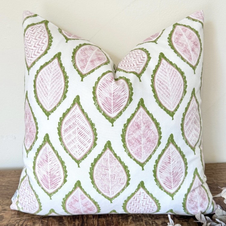 Pear green leaf print cushion cover with pink detailing on a wooden bench