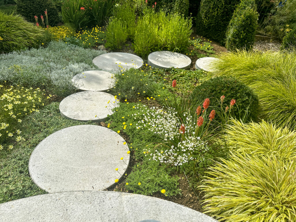 Curved concrete stepping stone path through low-maintenance grasses and planting, garden path ideas
