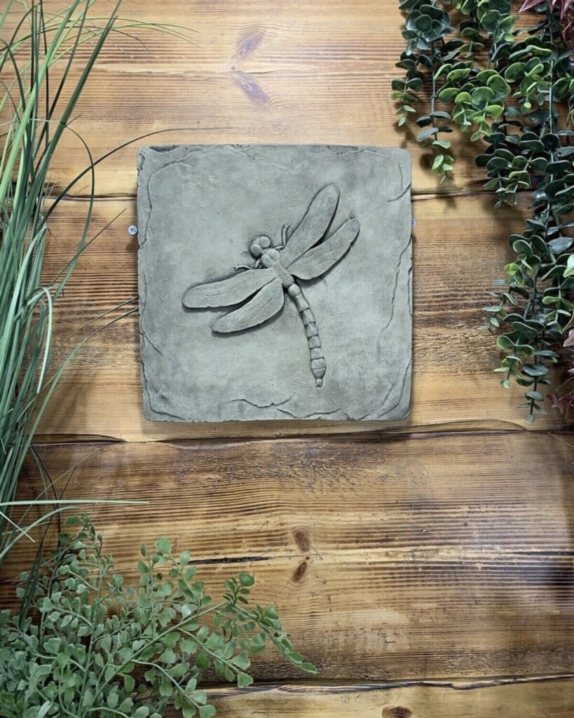 Stone dragonfly wall plaque mounted on wooden fencing with trailing plants