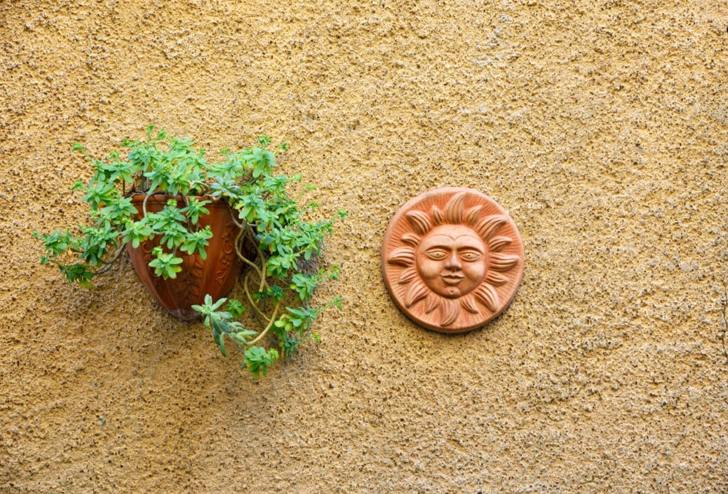 Terracotta ceramic sun face plaque and wall planter on a rendered garden wall