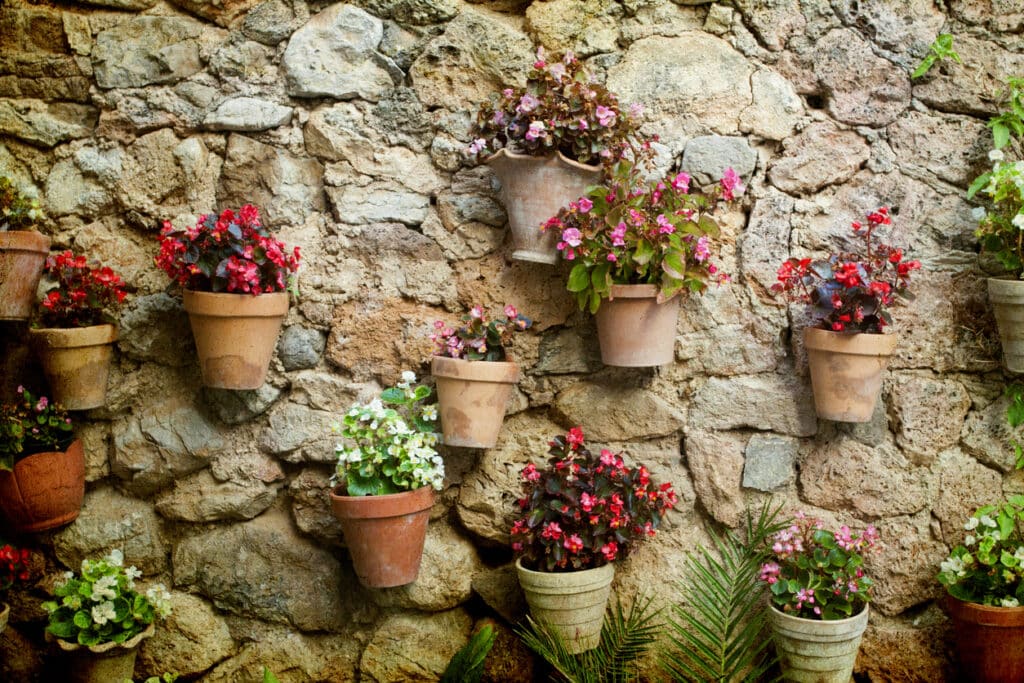 Terracotta pots of pink and red flowers mounted on a stone garden wall