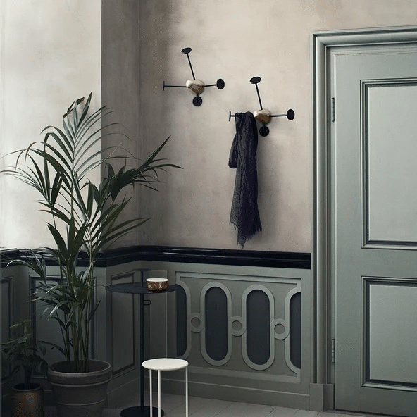 GUBI Mategot brass and black coat hooks mounted individually on panelled wall, with scarf and plant in hallway
