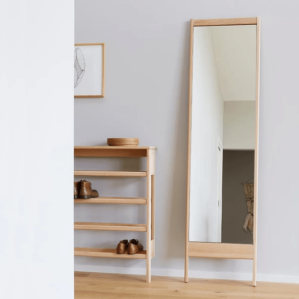 Oak-framed leaning mirror beside wooden shoe rack in a hallway entryway