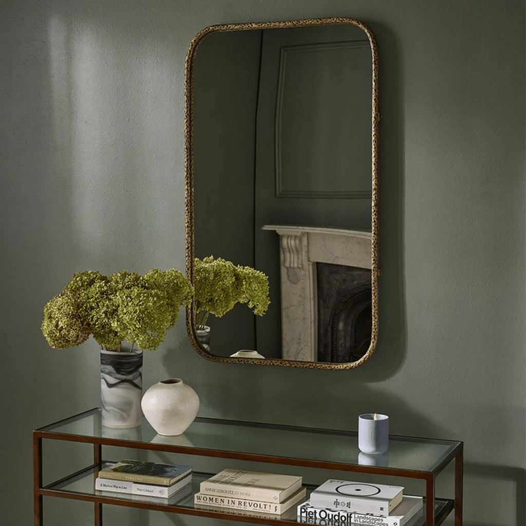 Arched brass-framed mirror above console table against sage green hallway wall