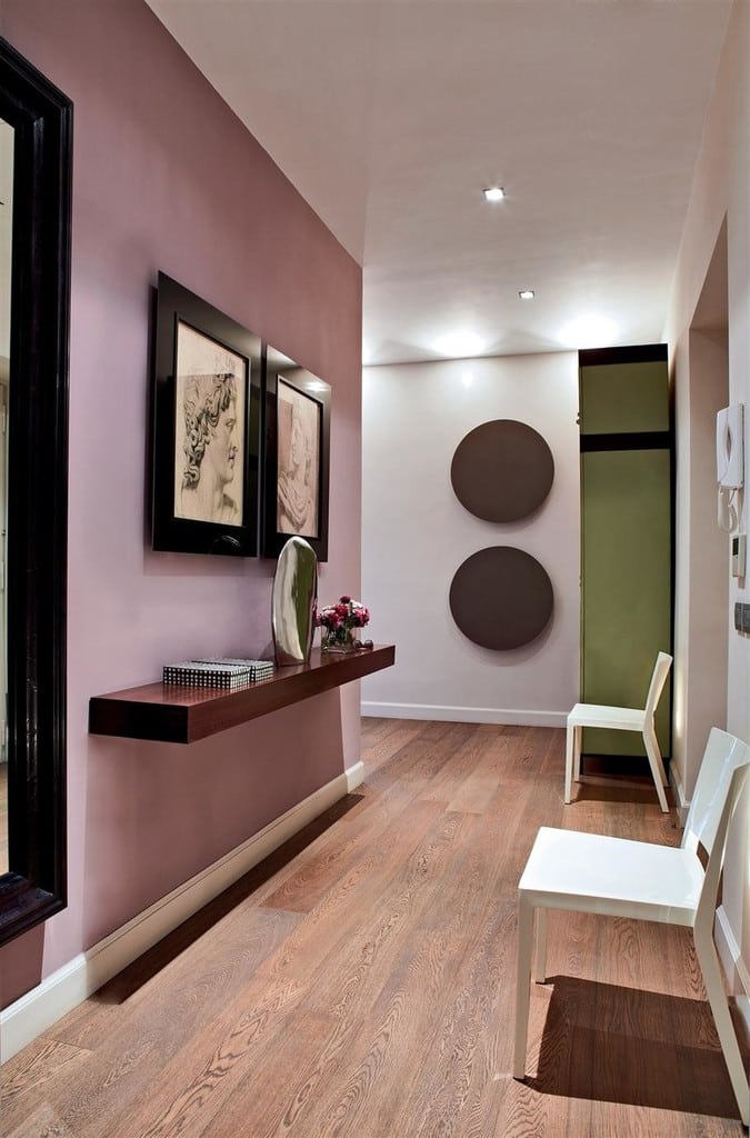 Pink hallway with dark wood floating console table, framed artwork and green door in a modern corridor