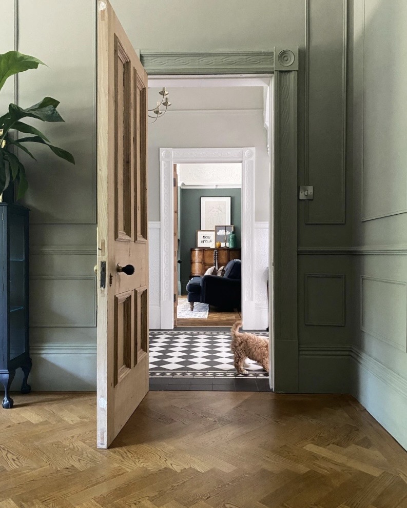 Sage green panelled hallway with parquet flooring and open door to living room