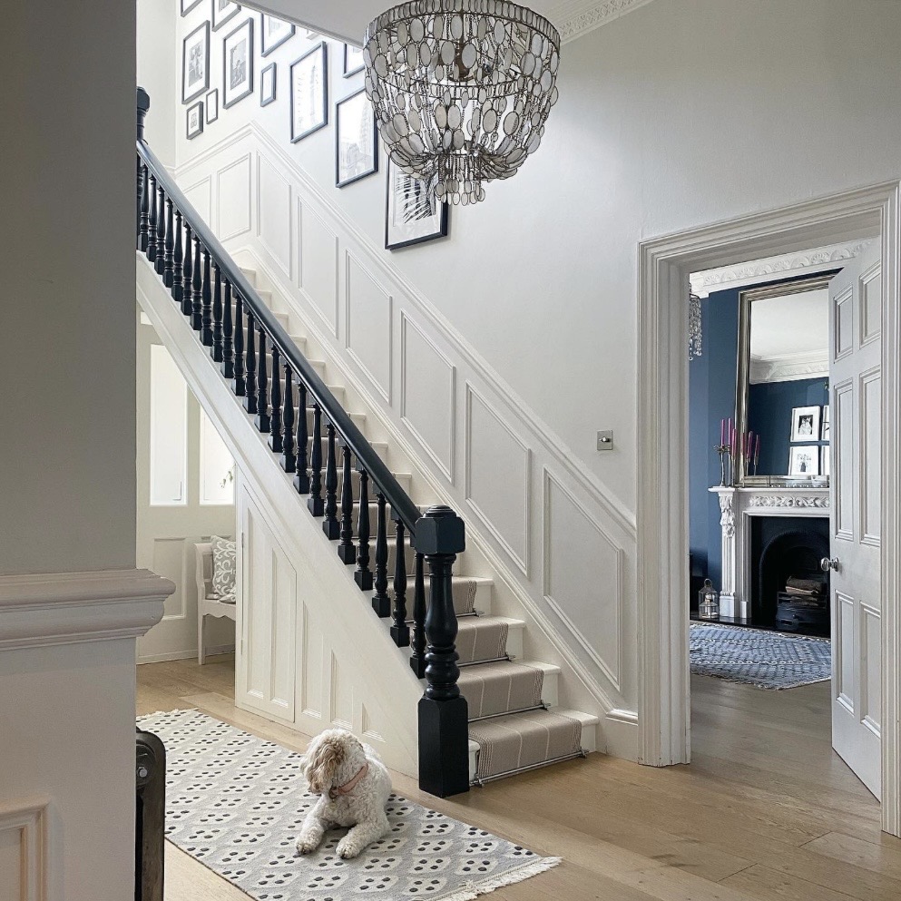 White wainscoting staircase with black balustrade and beaded chandelier