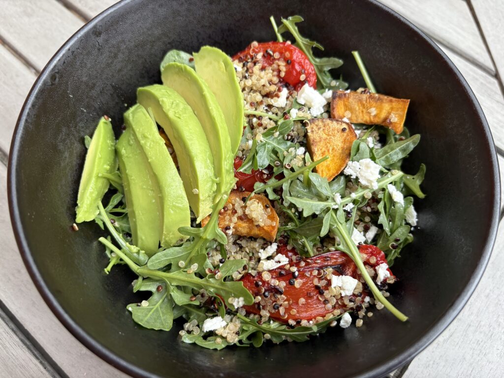 Quinoa salad with feta, roasted sweet potato, avocado, roasted peppers and rocket in a black bowl