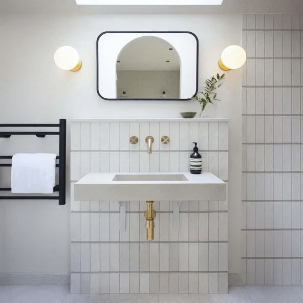 Tala Lochan graphite bathroom wall light above a concrete vanity with arched mirror and white ribbed tiling
