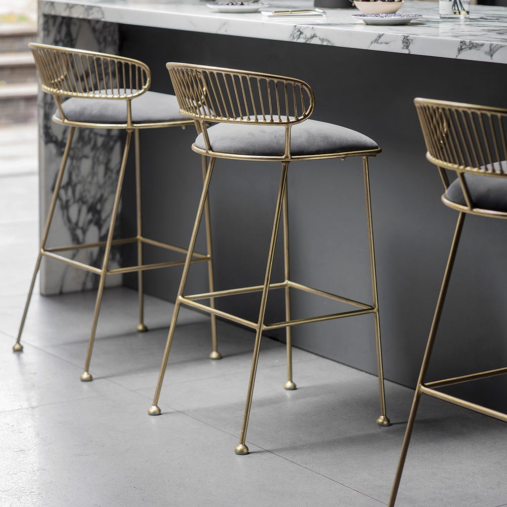 Brass wire bar stools with grey velvet seats at a marble kitchen island