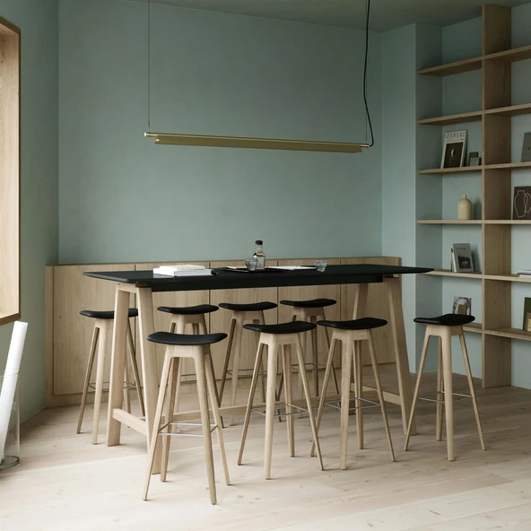 Pale oak stools with black upholstered seats around a high table in a sage green room