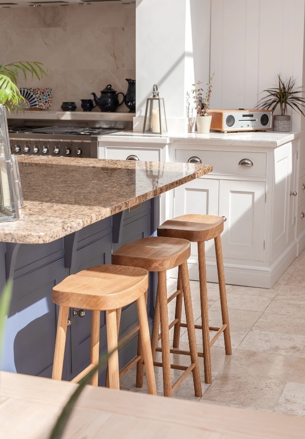 Three backless oak stools with saddled seats at a granite-topped kitchen island