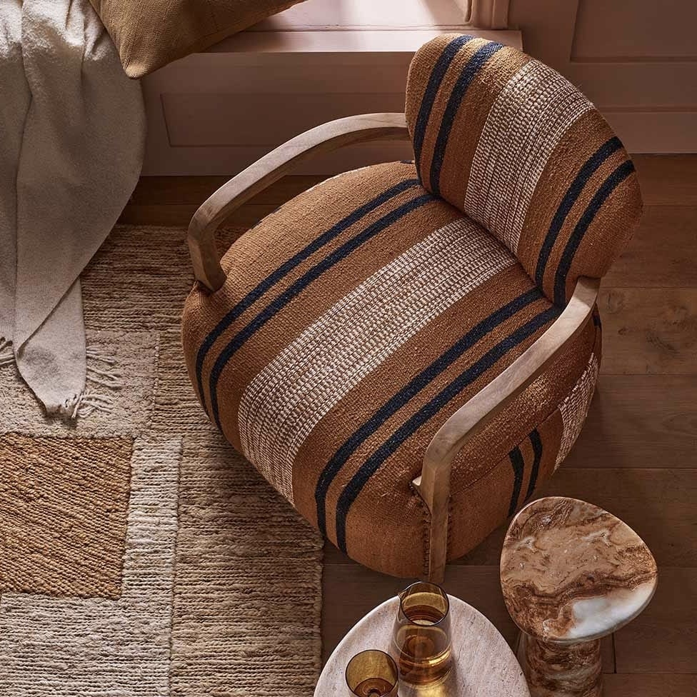 Aviator striped accent armchair in rust, navy and cream woven cotton rug fabric with curved timber arms, beside a marble side table