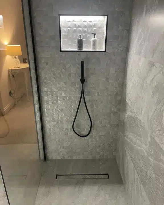 Lit shower niche lined with Cubik Indic relief tiles above a matt black shower set and linear drain
