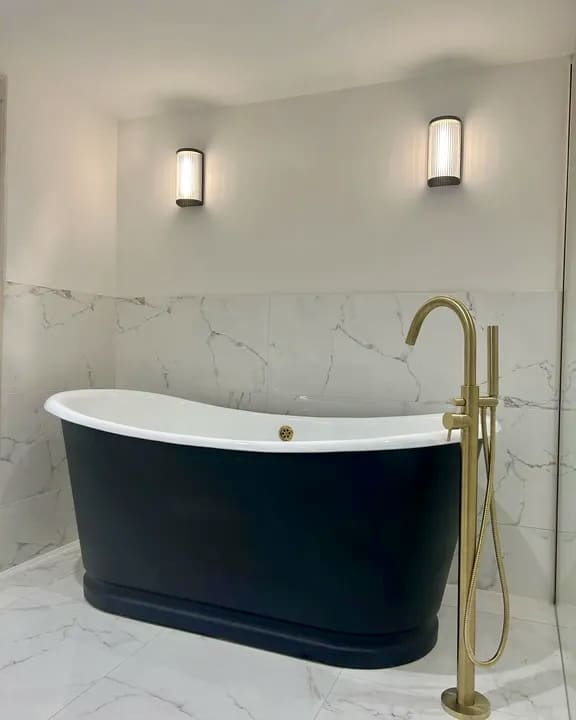 Half-height marble-effect wall tiles behind a navy roll-top bath with a brass floor-standing tap