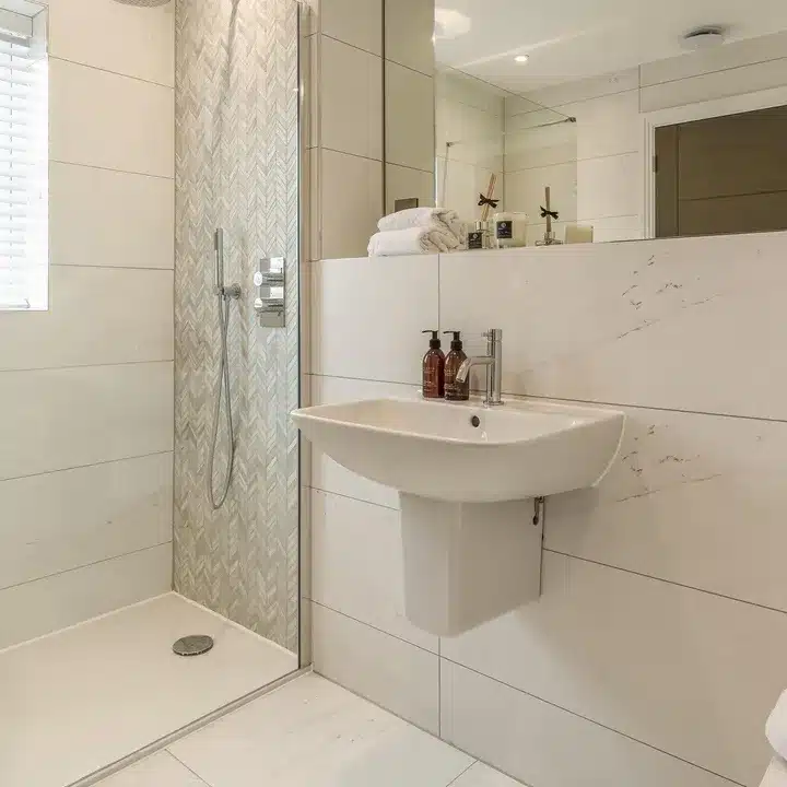Cream marble-effect wall tiles with a herringbone mosaic shower wall and wall-hung basin