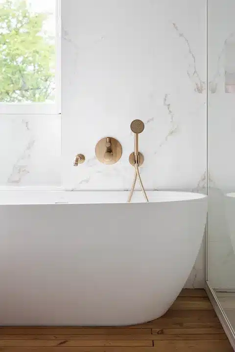 White freestanding bath against gold-veined marble-effect tiles with brushed brass fittings