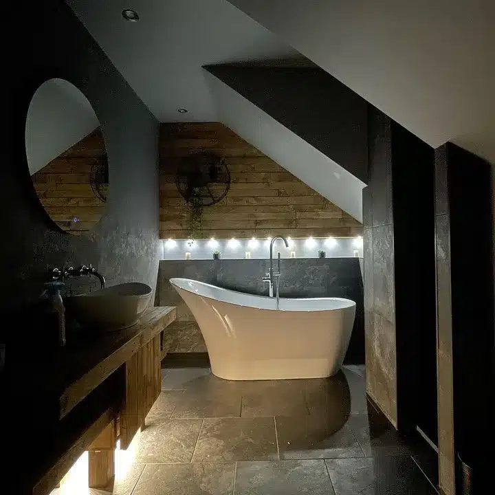 Dark stone-effect loft bathroom at night lit by LED strips beneath reclaimed timber cladding