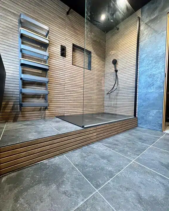 Dark slate-effect floor tiles with a raised timber-clad shower platform and slatted wood-effect walls