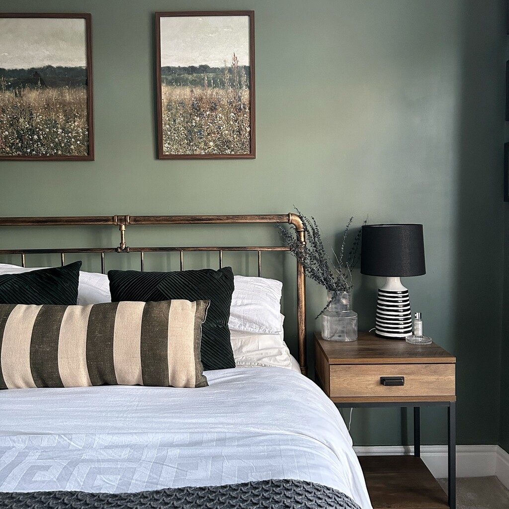 Green and black bedroom with Farrow & Ball Green Smoke walls, an antique brass bed, a black lamp and striped cushions