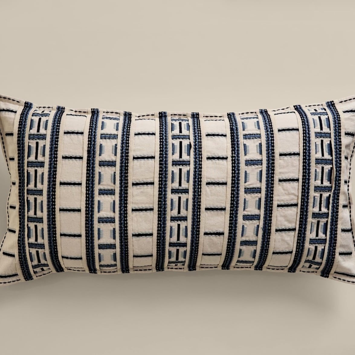 Blue embroidered grid bolster cushion adding contrast to a beige boho bedroom